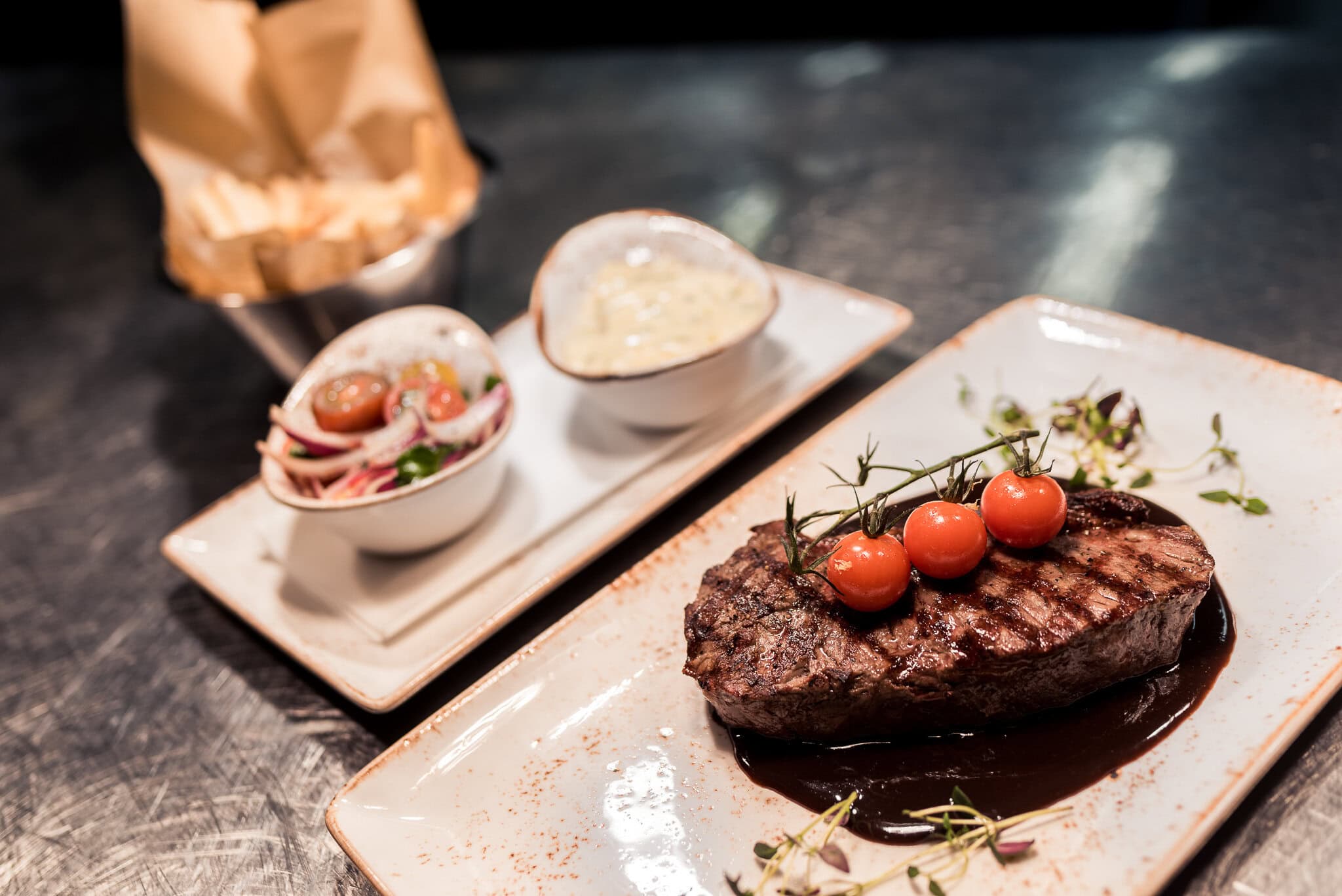 Juicig stek med tomater och balsamico på tallrik, serverad med sallad och såser, på restaurang i Stockholm.