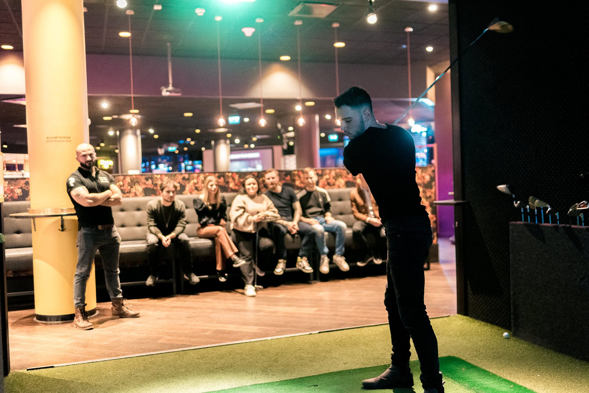 _DSC9262 Skjutspel på inomhusgolfcenter, golfputting med golfklubba och golfboll för underhållning och social aktivitet. Människor som spelar golf inomhus, golfentusiaster och golfträning i en modern miljö.