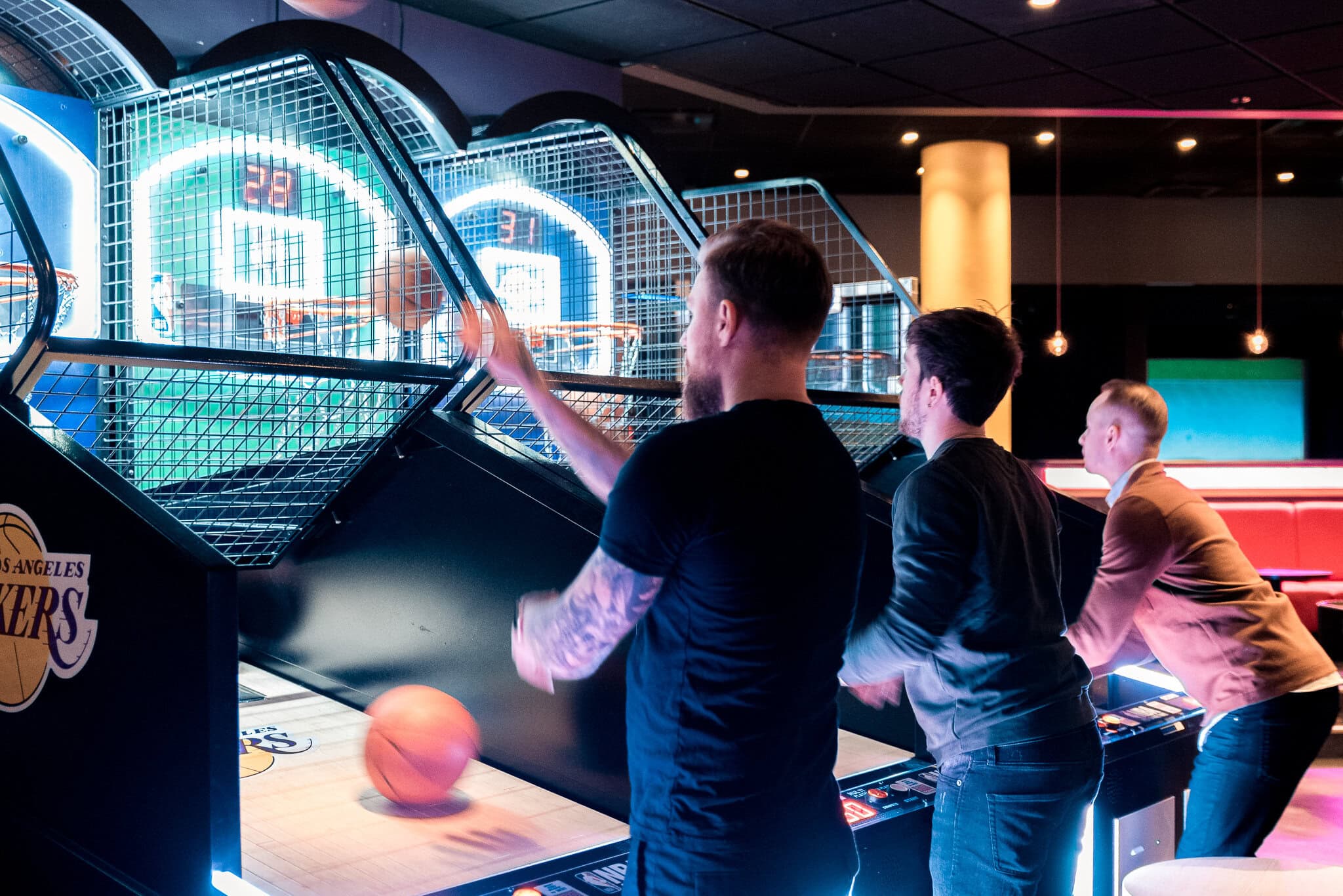 _DSC9164 Spelare som spelar basket på amerikansk arkadspel i en nöjeshall, med neonbelysta skärmar och glada ansikten. Perfekt för actionfyllda foto och bild av nöje och underhållning.