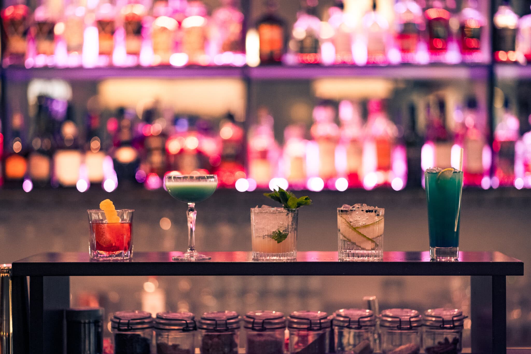 _DSC9640 Kreativa cocktails på en bar med färgglada ljus i bakgrunden, perfekt för en kvällsdrink och sociala tillställningar.