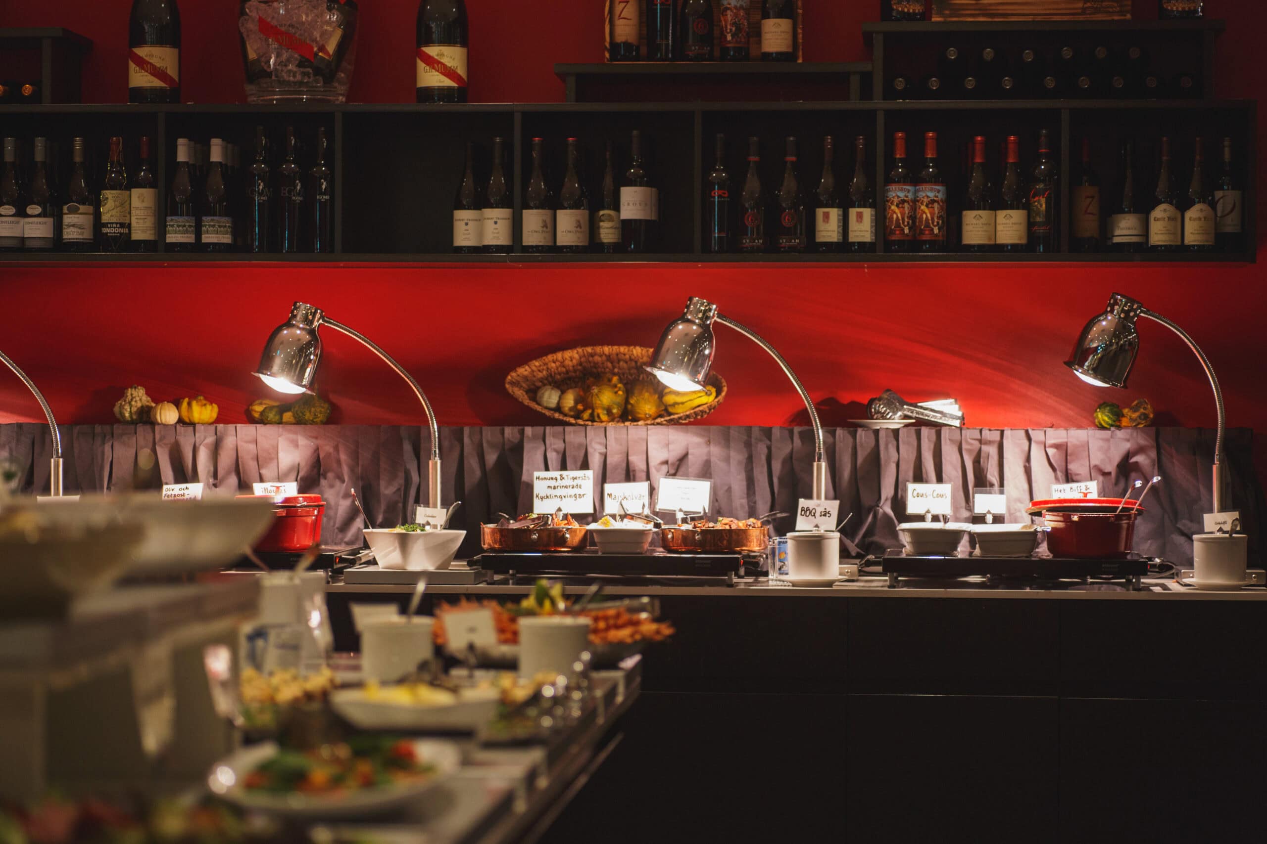 Ljusmontörsbelyst buffébord med varm mat och tillbehör, inomhusmiljö med vinflaskor på hyllor, på en restaurang eller festlokal, perfekt för att locka till sig matälskare.